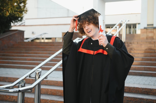 Podekscytowany doktorant w sukni z podniesionymi rękami trzyma dyplom