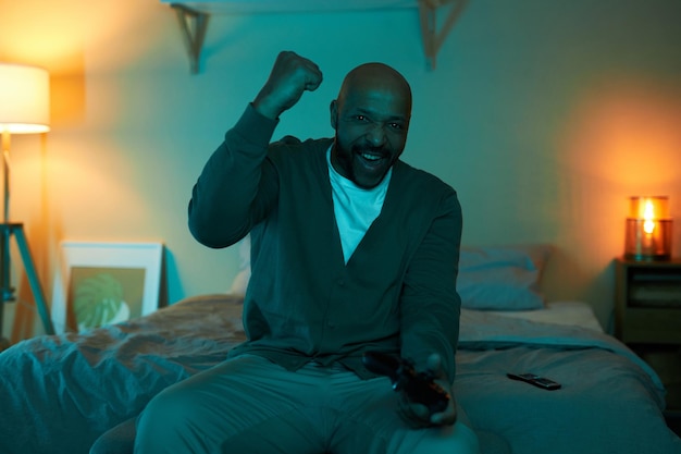 Zdjęcie podekscytowany dorosły czarny mężczyzna grający w gry wideo w ciemności i świętujący zwycięstwo