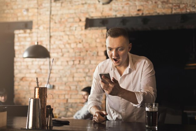 Podekscytowany kibic dopingujący wygraną w zakładach sportowych, świętujący wynik zwycięstwa, oglądający mecz online na smartfonie, wspierający zwycięską drużynę i pijący piwo w pubie