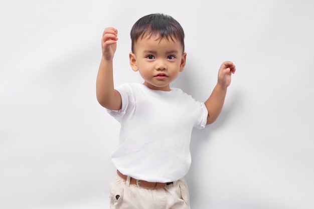 Podekscytowany mały azjatycki chłopiec w wieku 2 lat ubrany w białą koszulkę, podnoszący pięść, świętujący sukces odizolowany na białym tle