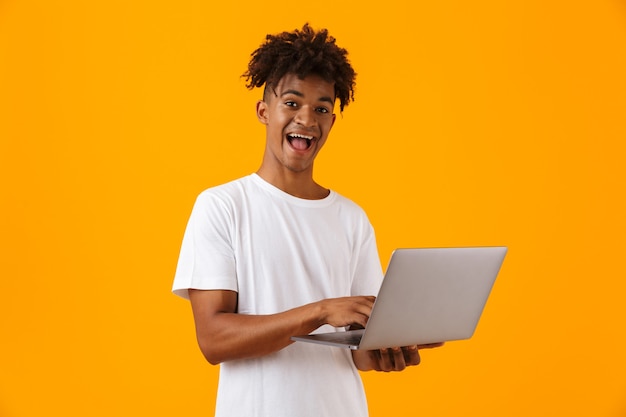 Podekscytowany młody człowiek Afryki samodzielnie nad żółtą przestrzenią za pomocą laptopa.