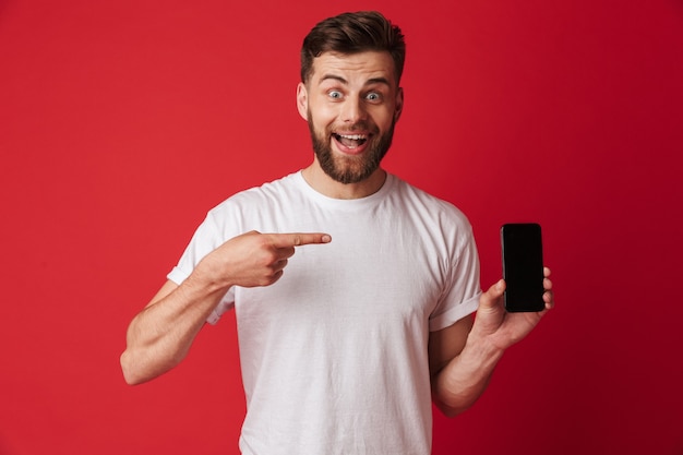 Podekscytowany młody człowiek wskazuje telefon komórkowy za pomocą telefonu komórkowego.