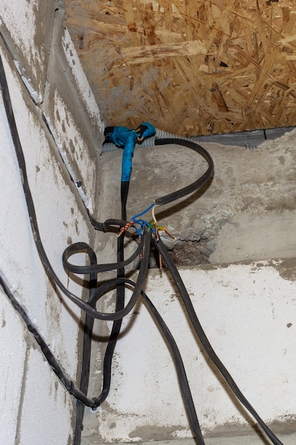 Podłączenie przewodów na tle ściany w domu w trakcie budowy. Skręcanie, lutowanie, spawanie kabli elektrycznych.