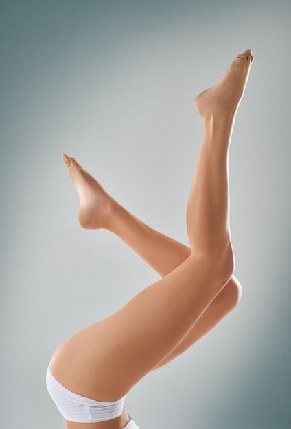 Podnoszenie nogi Przycięte zdjęcie studyjne przedstawiające nogi kobiety w powietrzu na szarym tle