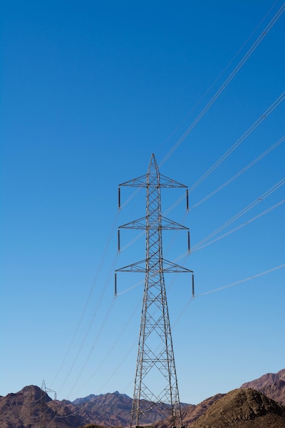 Podparcie elektryczne kabli elektroenergetycznych wysokiego napięcia. Metalowy wspornik z izolatorami wysokiego napięcia i na tle błękitnego nieba na pustyni ze wzgórzami i górami.