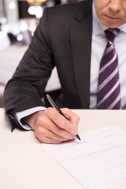 Podpisanie umowy. Zbliżenie: dojrzały mężczyzna w stroju formalnym, podpisujący dokument