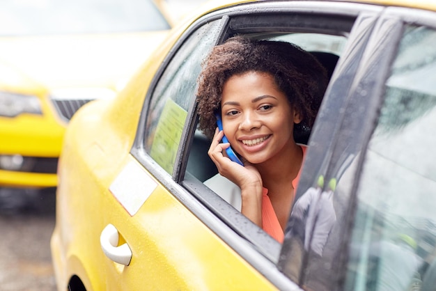 podróż służbowa, transport, podróże, gesty i koncepcja ludzi - młoda uśmiechnięta afroamerykanka dzwoniąca na smartfona w taksówce na ulicy miasta