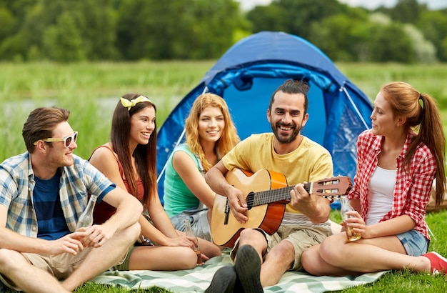 Podróż, turystyka, podwyżka, pinkin i ludzie pojęć, - grupa szczęśliwi przyjaciele z namiotem i napojami bawić się gitarę przy campingiem