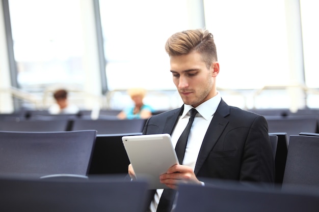 Podróże służbowe - biznesmen korzystający z cyfrowego tabletu w poczekalni odlotów na lotnisku