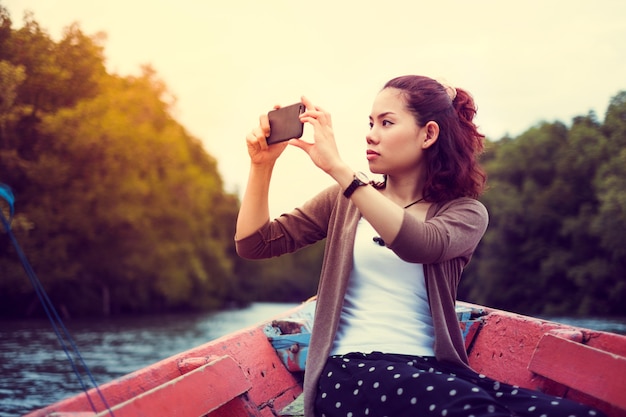 Zdjęcie podróżna kobieta używa mądrze telefon dla brać fotografię na łodzi przy wschodem słońca