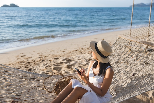 Podróżniczka Azjatka przy użyciu telefonu komórkowego i relaks w hamaku na plaży w Koh Chang Trad Tajlandia