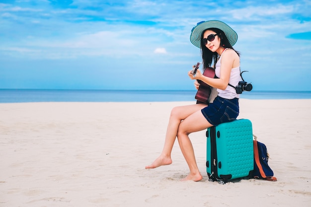 Podróżnik kobieta ma bagaż i gra na gitarze na plaży