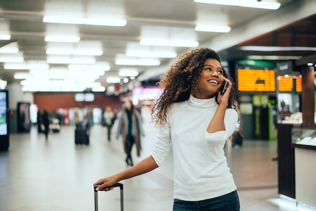 Podróżnik kobieta rozmawia przez telefon w terminalu lotniska z bagażem torby podróżnej.