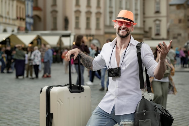 Podróżnik mody turystyczny turysta mężczyzna w moda kapeluszowych cajgach i okularach przeciwsłonecznych z walizką chodzi na s