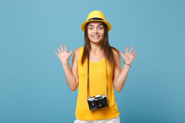 Podróżnik turystyczny kobieta w żółtych letnich ubraniach casual, kapelusz z aparatem fotograficznym na białym tle na niebieskiej ścianie. Pasażerka podróżująca za granicę w celu wyjazdu na weekend. Koncepcja podróży lotem lotniczym.