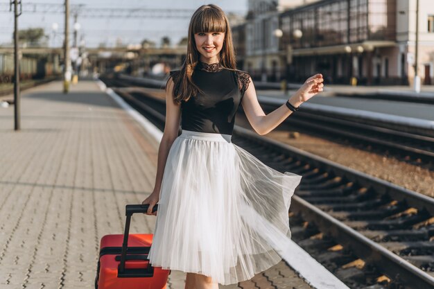 Podróżnik z czerwoną walizką w białej spódnicy czekający na pociąg na dworcu