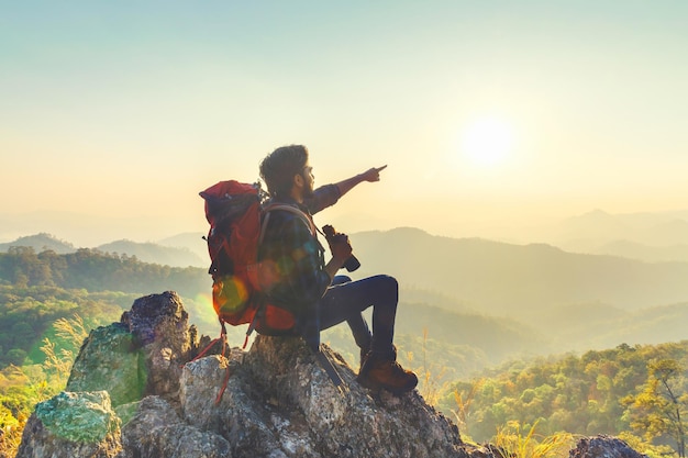Podróżnik z plecakiem i trzymający lornetkę siedzący na szczycie góry, wskazujący na widok