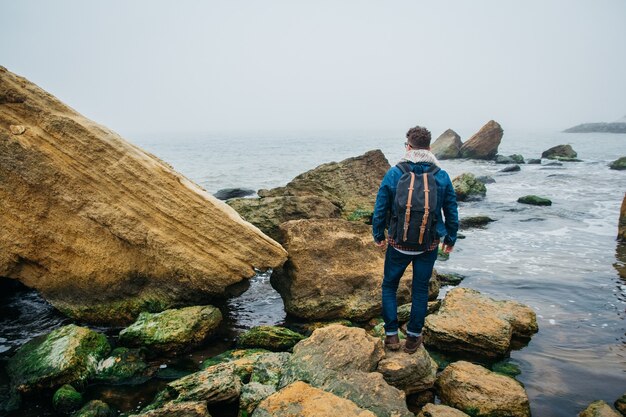 podróżnik z plecakiem stoi na skale na tle pięknego morza z falami