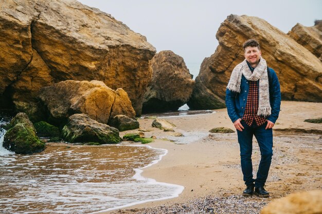 Podróżnik z plecakiem stojący na piaszczystej plaży pośrodku skał na tle morza