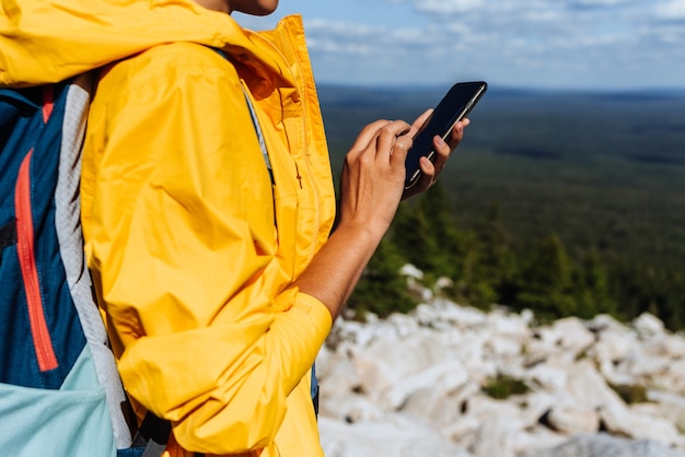 Podróżnik z telefonem, zbliżenie. Młoda kobieta ubrana w żółtą wiatrówkę użyj mapy wyszukiwania smartfona na tle wsi. Dorosła kobieta trzyma i używa smartfona. Podróże i aktywny tryb życia