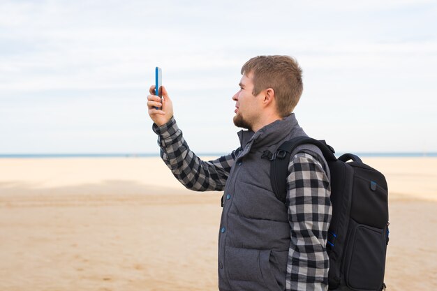 Podróżny człowiek robi zdjęcia na plaży aparatem w smartfonie podczas letnich wakacji lub wędrówki
