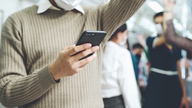 Podróżny noszący maskę na twarz podczas korzystania z telefonu komórkowego w pociągu publicznym