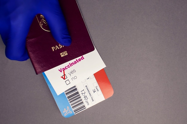 Zdjęcie podróżowanie podczas pandemii covid-19, ręka trzymająca paszport z biletem lotniczym, zaszczepiona karta covid-19 ze znakiem „tak” na szarym tle, koncepcja kontroli bezpieczeństwa i higieny pracy na lotnisku