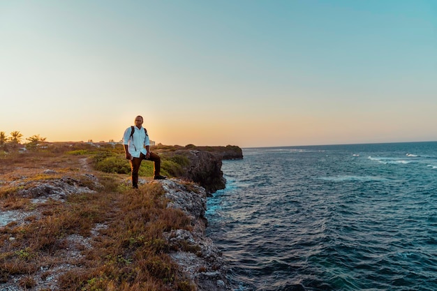 Podróżuj afrykański mężczyzna stojący na klifie oceanu, ciesząc się widokiem na zachód słońca