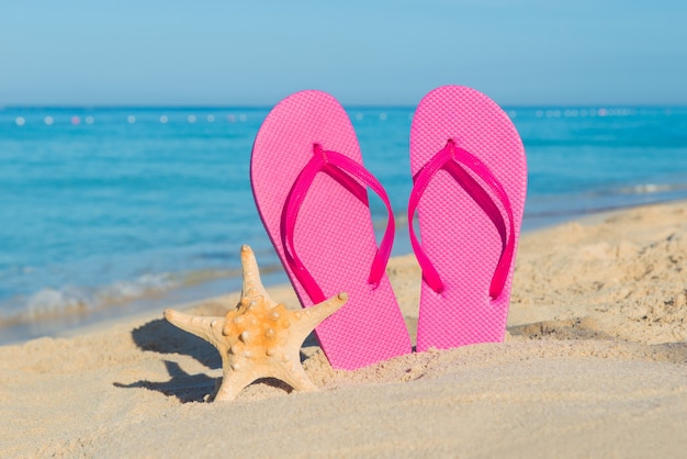 Podróżuj drogą morską. Wakacje na plaży. Różowe klapki i rozgwiazdy na piaszczystym wybrzeżu.