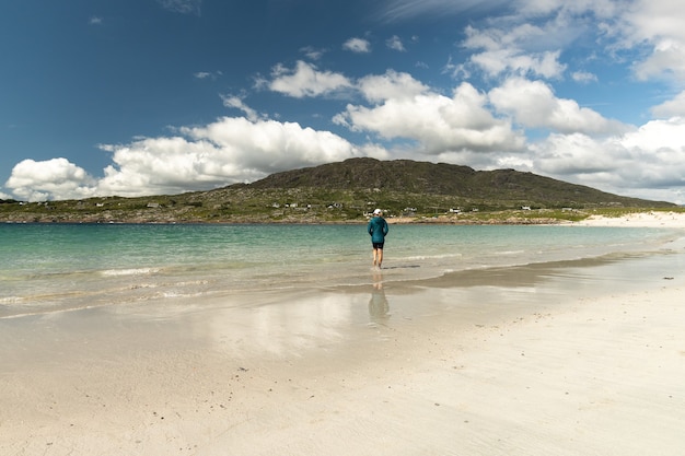 Podróżująca kobieta spacerująca wzdłuż białej, piaszczystej plaży i czystej wody w Dog's Bay Galway, Irlandia