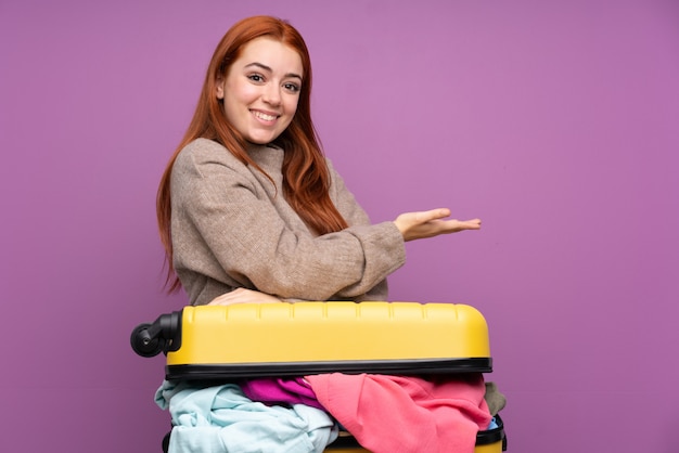 Podróżująca nastolatka z walizką pełną ubrań rozkładających ręce na bok, zapraszając do siebie