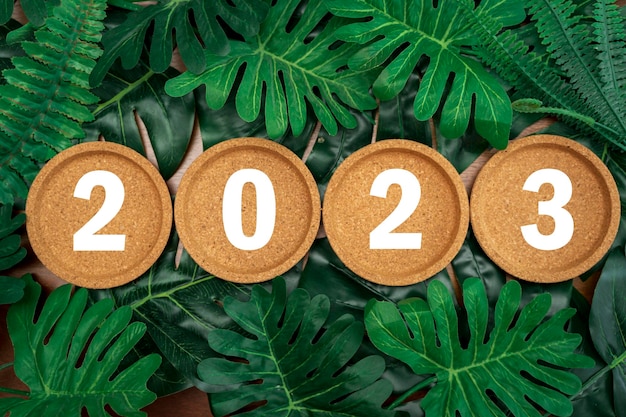 Podstawki korkowe na tle liści tropikalnych 2023 Szczęśliwego Nowego Roku z dekoracyjną latarnią świąteczną na liściu