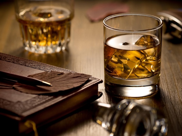 Podświetlana szklanka whisky na skałach na drewnianym stole z długopisem i drugą szklanką