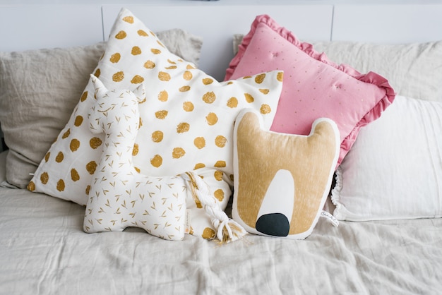 Poduszki w kształcie jednorożca i lisa oraz różowo-białe z żółtym groszkiem na łóżku