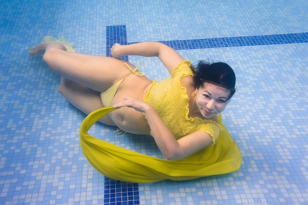 Podwodna kobieta w ciąży ubrana w sukienkę w głębokim basenie Dziewczyna pływa nurkowanie w basenie Aqua fitness Zajęcia zdrowotne dla kobiet w ciąży Trening terapii wodnej Najbezpieczniejsza i najskuteczniejsza forma ćwiczeń