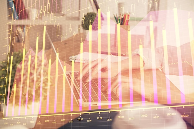 Podwójna ekspozycja rąk kobiety wpisując na komputerze i wykresie forex hologram rysujący koncepcję inwestowania na giełdzie