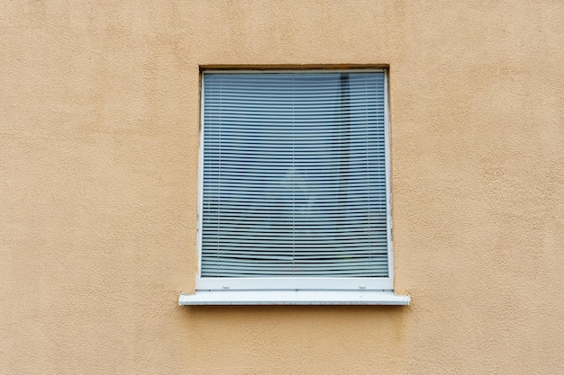 Podwójnie oszklone okno z zamkniętymi żaluzjami na pomarańczowej ścianie Zamknięte okno w domu Zewnętrzna część budynku mieszkalnego jest pomarańczowa