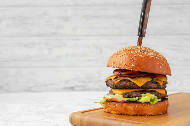 Podwójny cheeseburger podawany na drewnianej desce na białym niewyraźnym tle