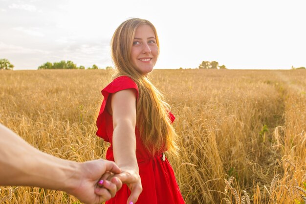 Zdjęcie pójdź za mną, piękna młoda kobieta trzyma rękę mężczyzny na polu pszenicy.