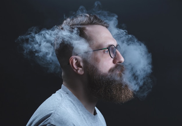Pojęcie. Dym ogarnął głowę mężczyzny. Portret brodaty, stylowy mężczyzna z dymem. Bierne palenie.
