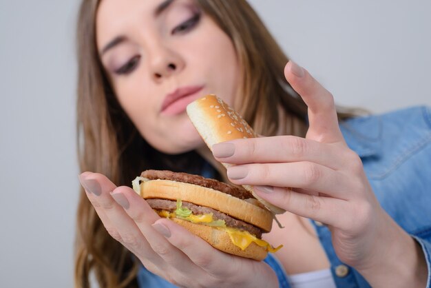 Pojęcie niezdrowego odżywiania. Zbliżenie na zdjęcie ciekawskiej kobiety patrzącej wewnątrz dużego tłustego hamburgera