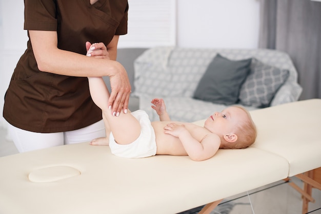 Pojęcie opieki zdrowotnej i medycznej. Profesjonalna masażystka wykonuje masaż i gimnastykę dla małego dziecka w nowoczesnym przytulnym pokoju.