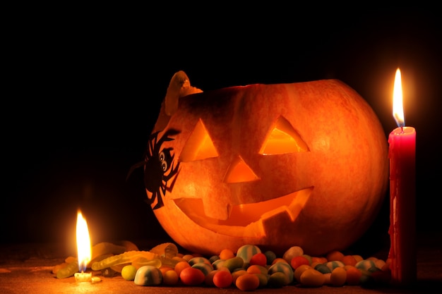 Pojęcie święta Halloween. Halloweenowa głowa dyni ze świecami wewnątrz i wokół na drewnianym stole na czarnym tle