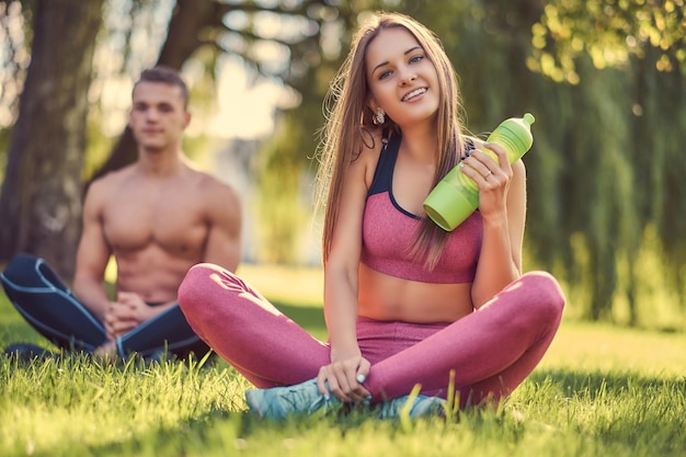 Pojęcie zdrowego stylu życia. Szczęśliwa młoda para fitness siedzi w pozycji lotosu na zielonej trawie.