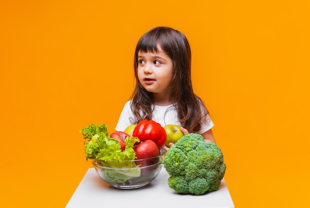 Pojęcie żywności ekologicznej mała dziewczynka trzyma kosz owoców i warzyw na żółtym tle Zdrowe jedzenie dla dzieci