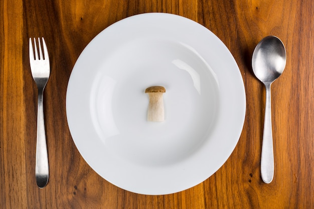 Zdjęcie pojedyncza pieczarka na białym spodeczku na drewnianym stole