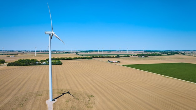 Pojedyncza turbina wiatrowa stojąca na brudnym polu z odległymi zielonymi uprawami powietrznymi