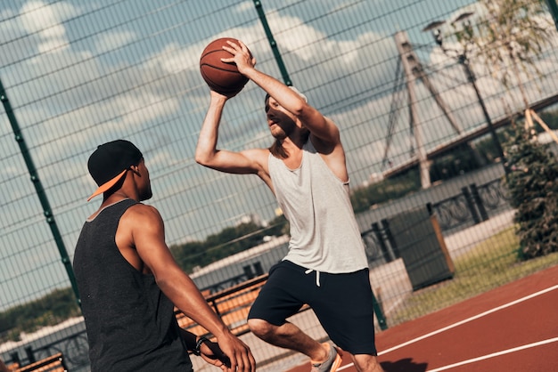 Pokazuje swój najlepszy strzał. Dwóch młodych mężczyzn w sportowej odzieży grających w koszykówkę podczas spędzania czasu na świeżym powietrzu