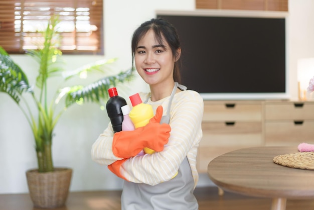 Pokojówka trzyma butelki do czyszczenia i pokazuje kciuk do góry po czyszczeniu i wycieraniu brudu w domu