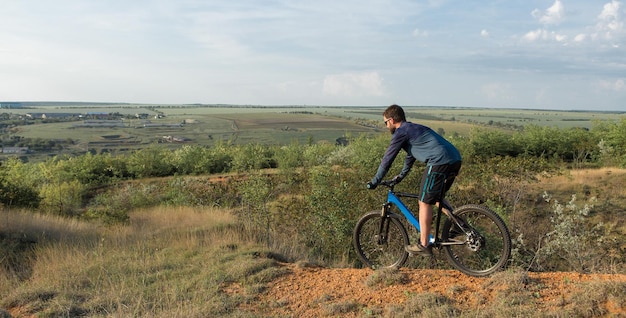 Pokonywanie górskich szczytów przez rowerzystę w krótkich spodenkach i koszulce na nowoczesnym rowerze hardtail z włókna węglowego z widelcem pneumatycznym Piękny widok z góry